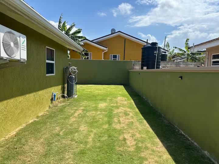 Enclosed side yard with grass and a view of the house wall